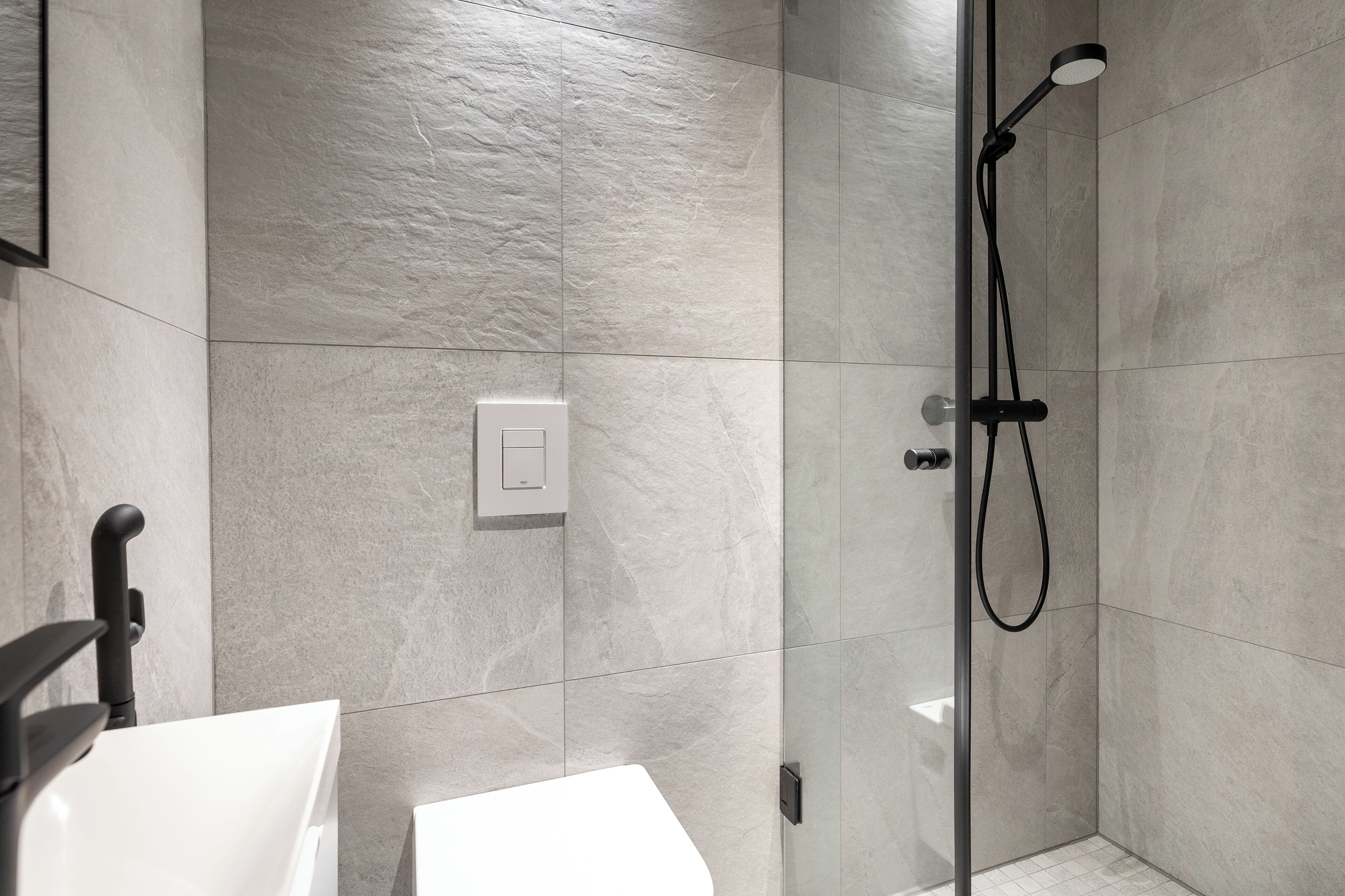 A modern bathroom with a glass-enclosed shower, a white sink, and a wall-mounted light switch.