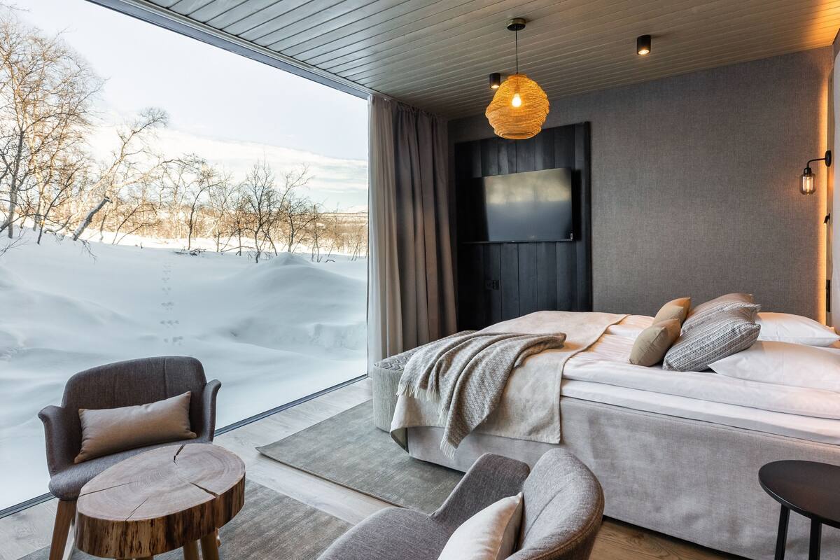 Une chambre moderne dotée d’une grande fenêtre, d’un lit, d’une télévision et d’un coin salon.