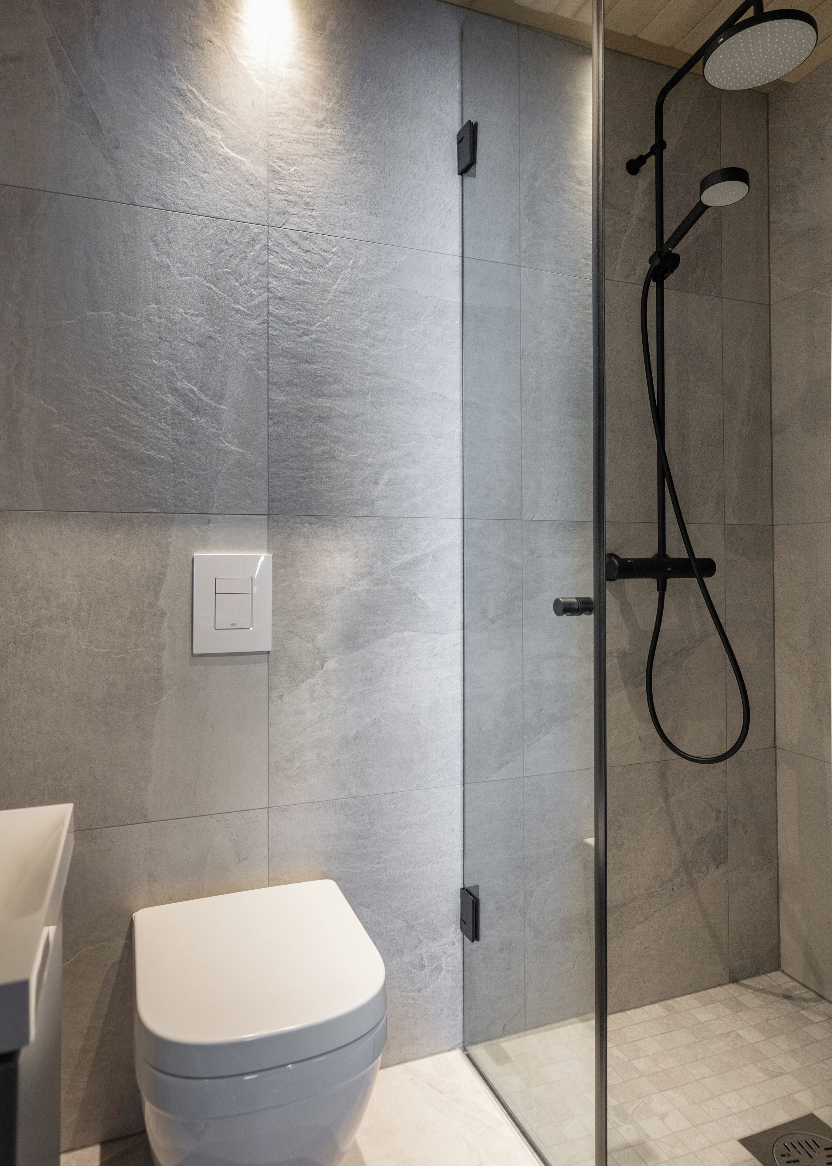 Une salle de bain moderne avec une douche à parois de verre, des toilettes blanches et un interrupteur fixé au mur.