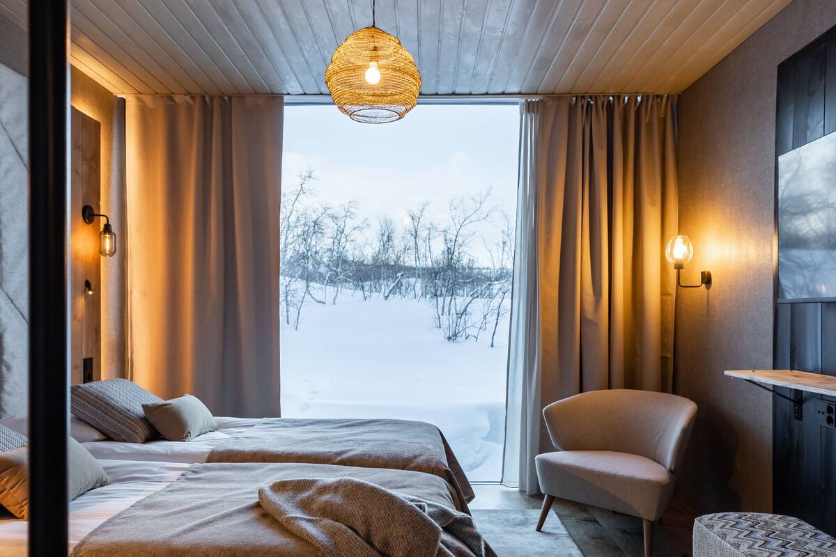 Une chambre moderne avec un grand lit, un fauteuil et une vue sur un paysage enneigé par une grande fenêtre.