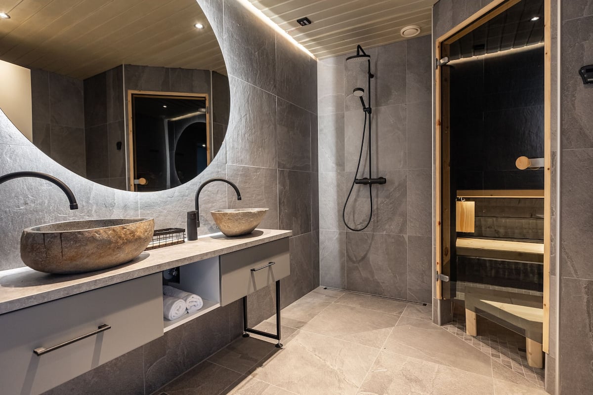 Une salle de bain moderne avec un grand lavabo en pierre, une douchette à main et un banc en bois.