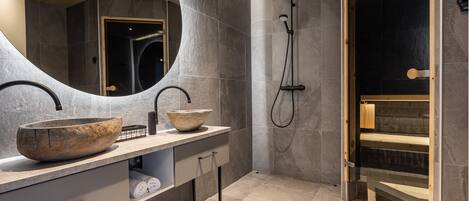A modern bathroom with two large stone sinks, a shower, and a wooden bench.
