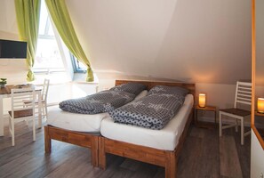 A bedroom with a wooden bed, a desk, a chair, and a TV mounted on the wall. - Pension Café Klingbeil (Glueckstadt)