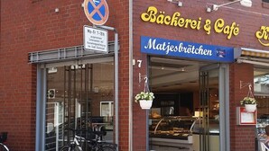 Un bâtiment en briques rouges abritant un café appelé « Bäcker & Café » et une boulangerie appelée « Matjesbröcken ».
