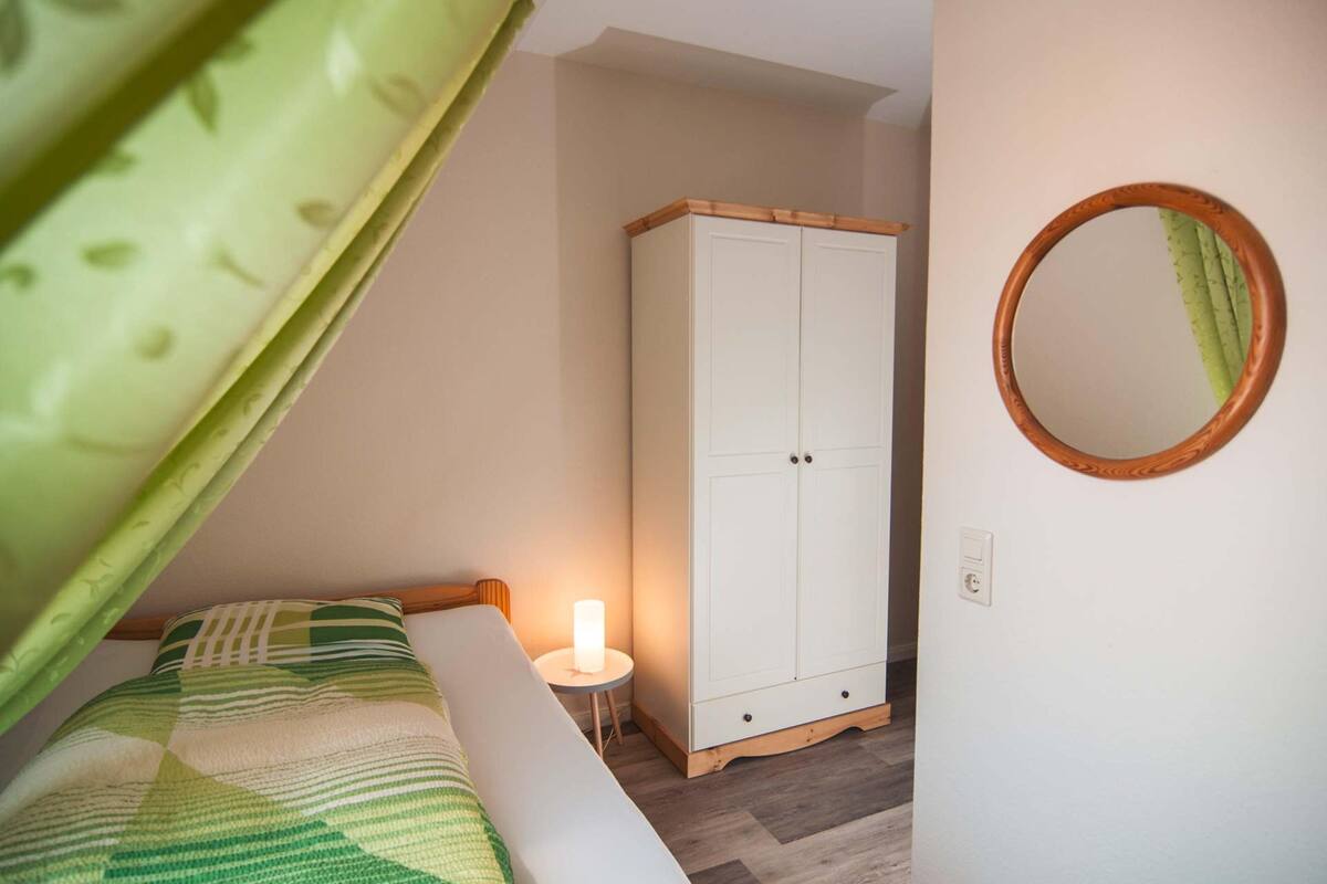 Une chambre à coucher avec un lit, une table de chevet avec une lampe, une armoire et un miroir au mur.