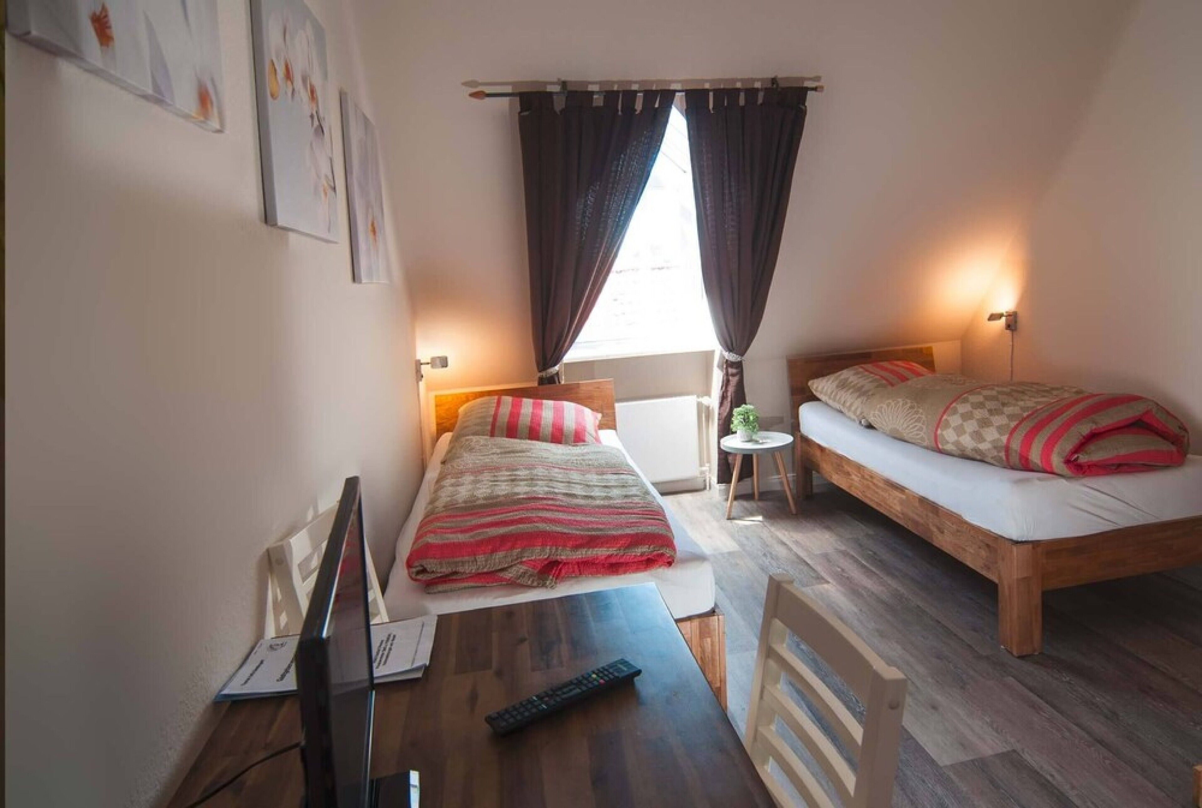 Een kleine, goed verlichte kamer met twee bedden, een bureau en een televisie.