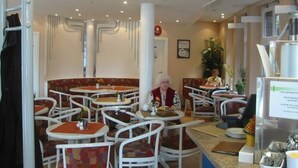 Un restaurant avec des tables et des chaises rondes, un comptoir où est affiché le menu, et une plante dans un coin.
