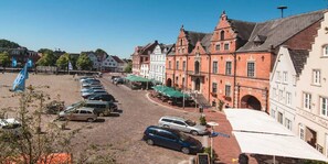 Eine gepflasterte Straße gesäumt von historischen Gebäuden, ein Parkplatz und Außenbereich für Cafés.