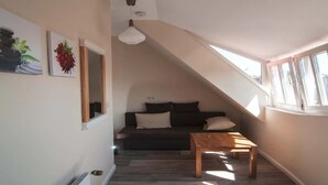 Une pièce de style « loft » avec un plafond en pente, un canapé de couleur sombre, une table basse en bois et deux tableaux accrochés au mur.