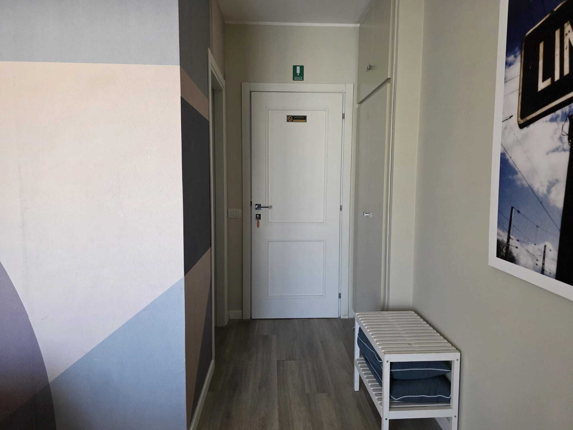 Un pasillo estrecho con una puerta blanca, un pequeño banco y un cartel en la pared.