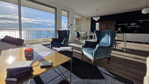 A modern living room with a large window overlooking a balcony, a dining area, and a kitchen. - Be Your Home - Guest House Seataly (Civitavecchia)