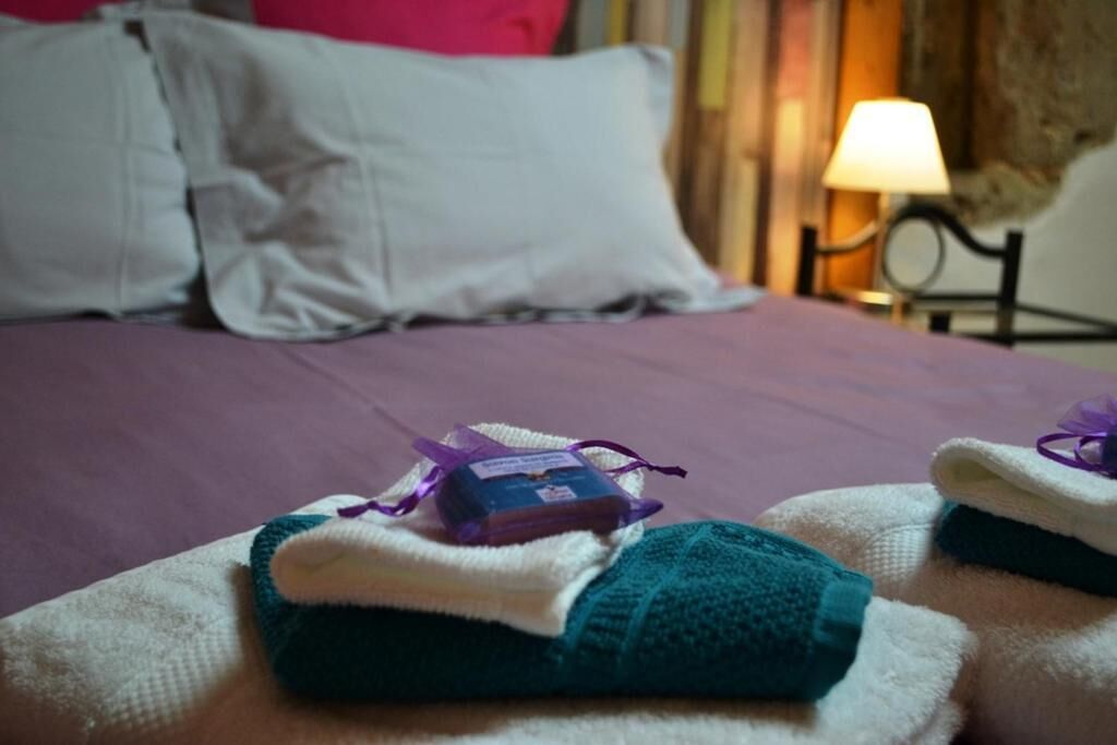 Una cama con un edredón morado, almohadas blancas y una mesita de noche con una lámpara.