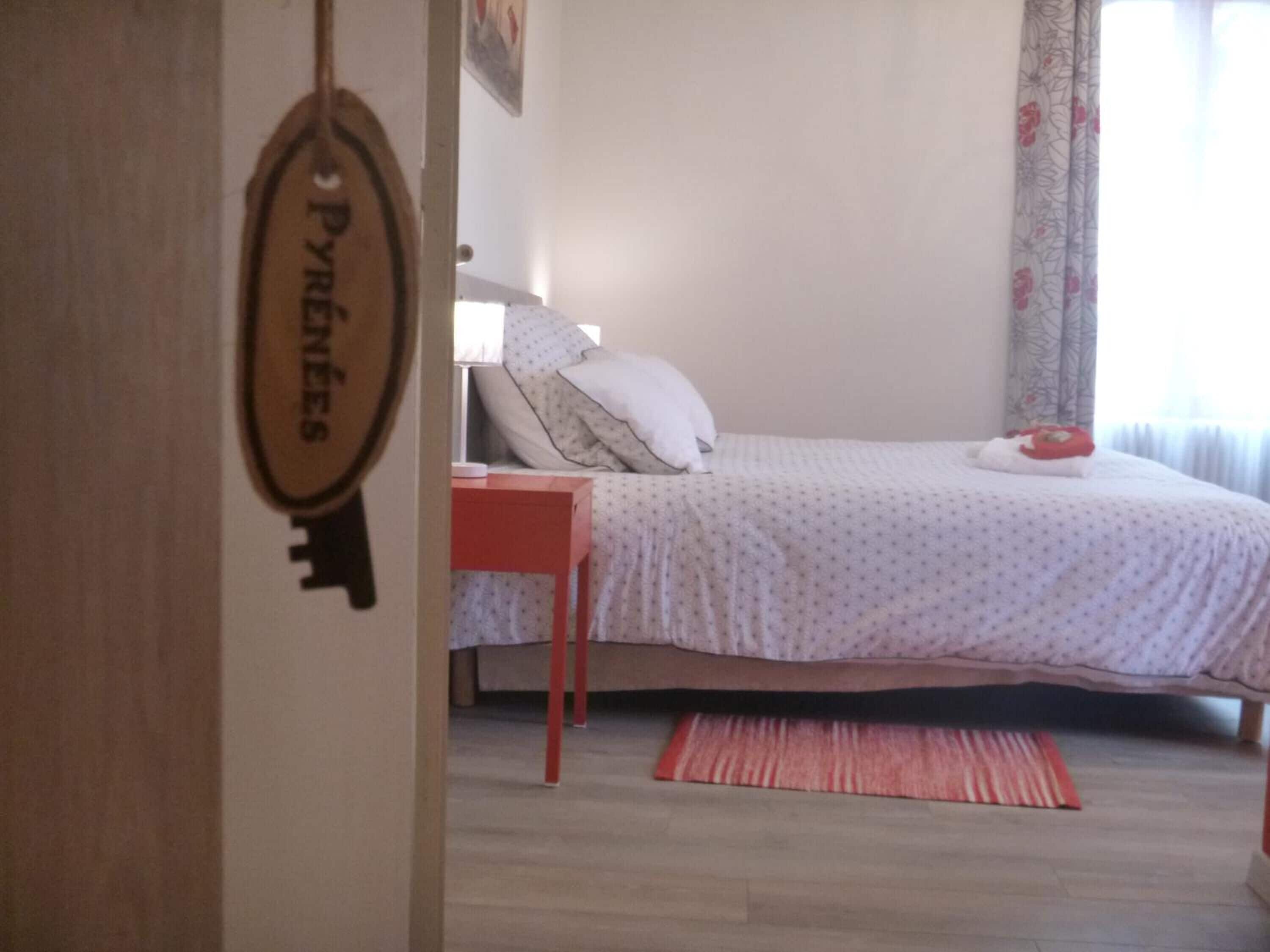 Un dormitorio con cama, una mesita de noche, una mesita auxiliar roja, una colcha estampada y una llave colgada en la pared.