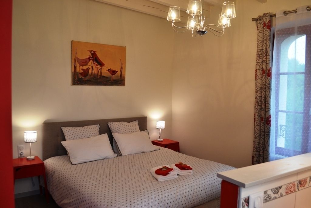 Una cama bien hecha con un edredón estampado, dos lámparas de noche y un cuadro en la pared.