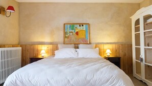 Un dormitorio con una cama grande, dos mesitas de noche con lámparas, un cabecero de madera, un radiador y un armario.