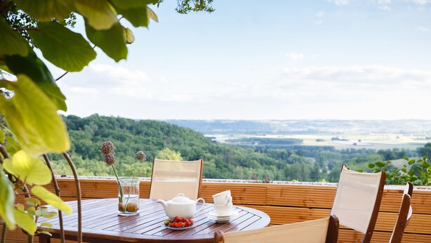 Mesa de madera con sillas en una terraza, con vistas a un paisaje boscoso.
