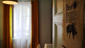Una habitación con ventana, cortinas y un adorno en la pared que muestra la palabra "Bee" e ilustraciones de abejas.
