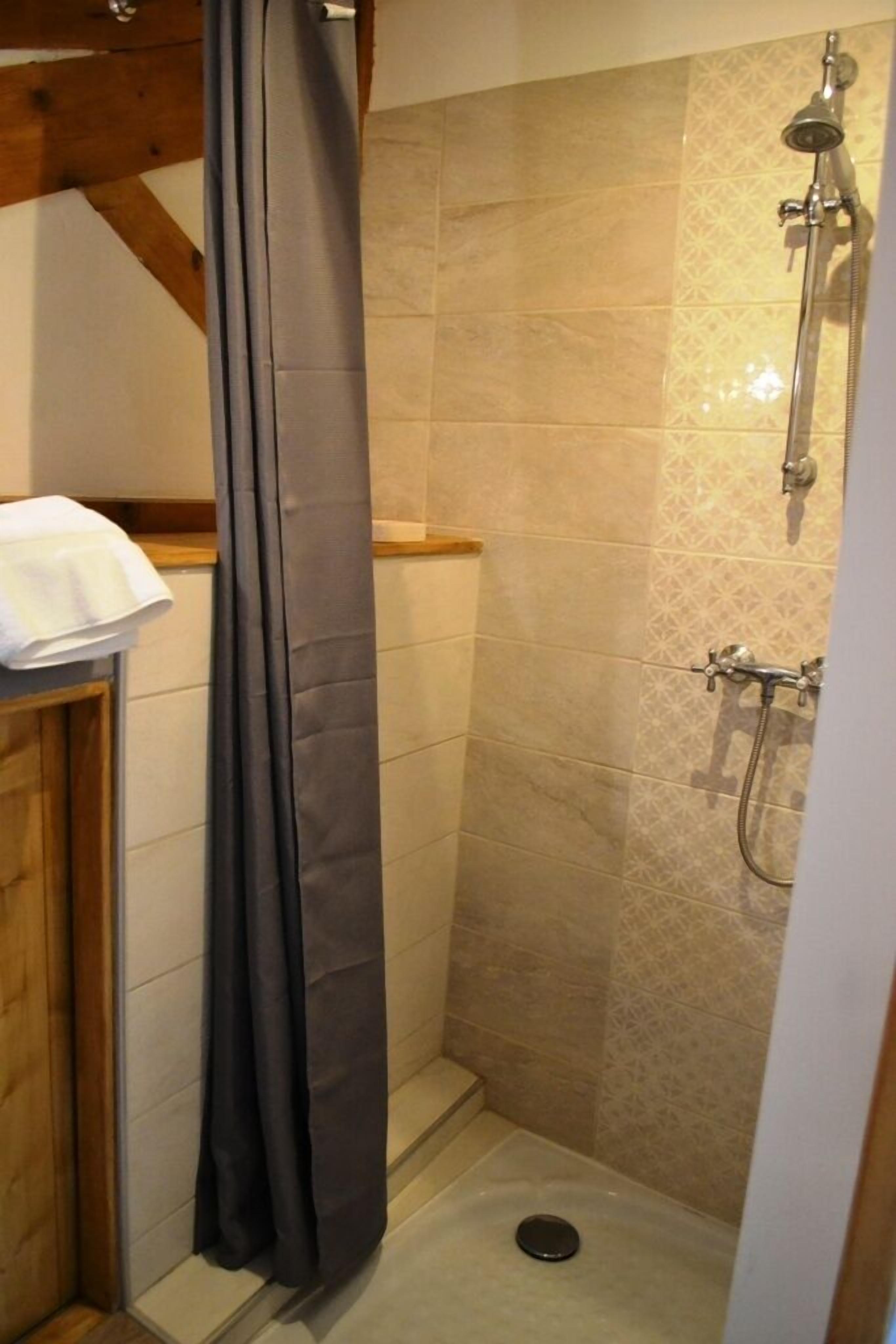A shower area with a showerhead, a curtain, and a towel on a wooden shelf.