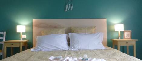 A neatly made bed with white linens, two pillows, and a dreamcatcher hanging above. There are two bedside tables with lamps and a framed picture on one.