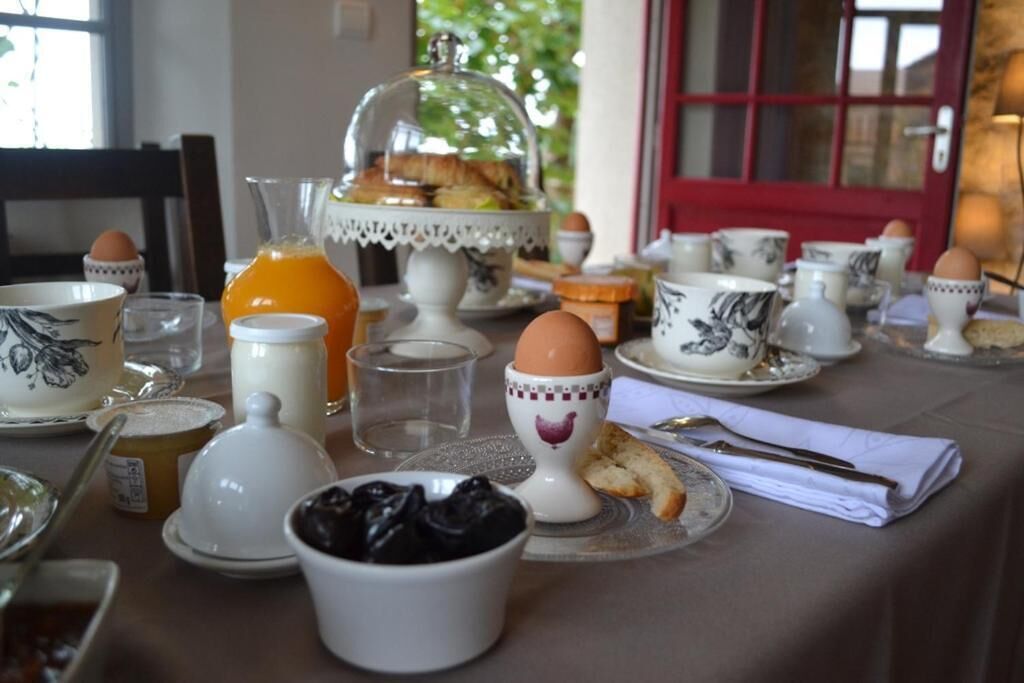 Une table mise pour le petit-déjeuner, avec une nappe et une place pour deux personnes, comprenant des assiettes, des bols, des tasses et un verre de jus d’orange.