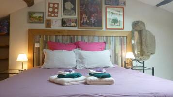 Quarto com cabeceira de madeira, cama com almofadas rosa e brancas, e parede decorada com quadros e obras de arte.