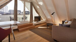 A modern loft apartment with a large skylight, a cozy living area with a sofa and TV, a dining table, and a view of the cityscape. - Hotel Gasthof zum Ochsen (Arlesheim)