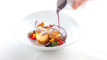 A dessert on a white plate with chocolate sauce being poured over it.