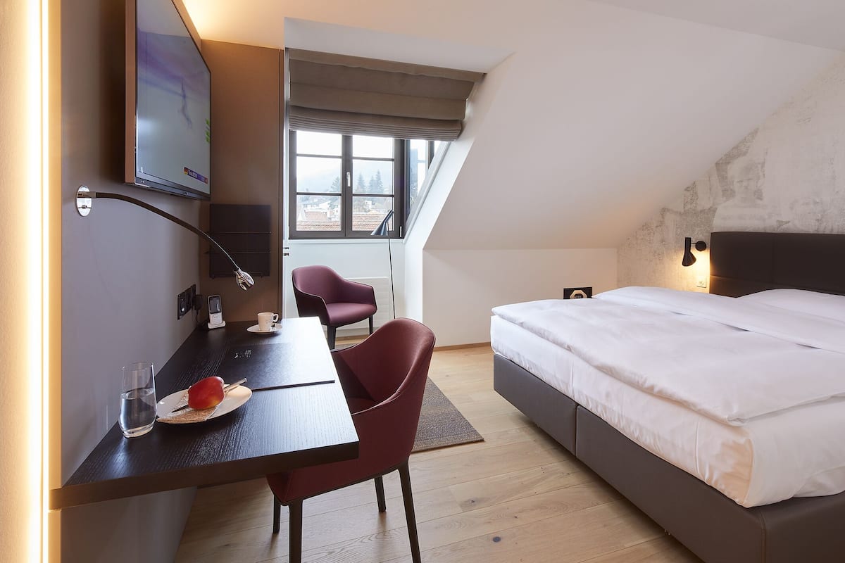 A modern hotel room with a bed, desk, and chair, a TV, and a window with a view.