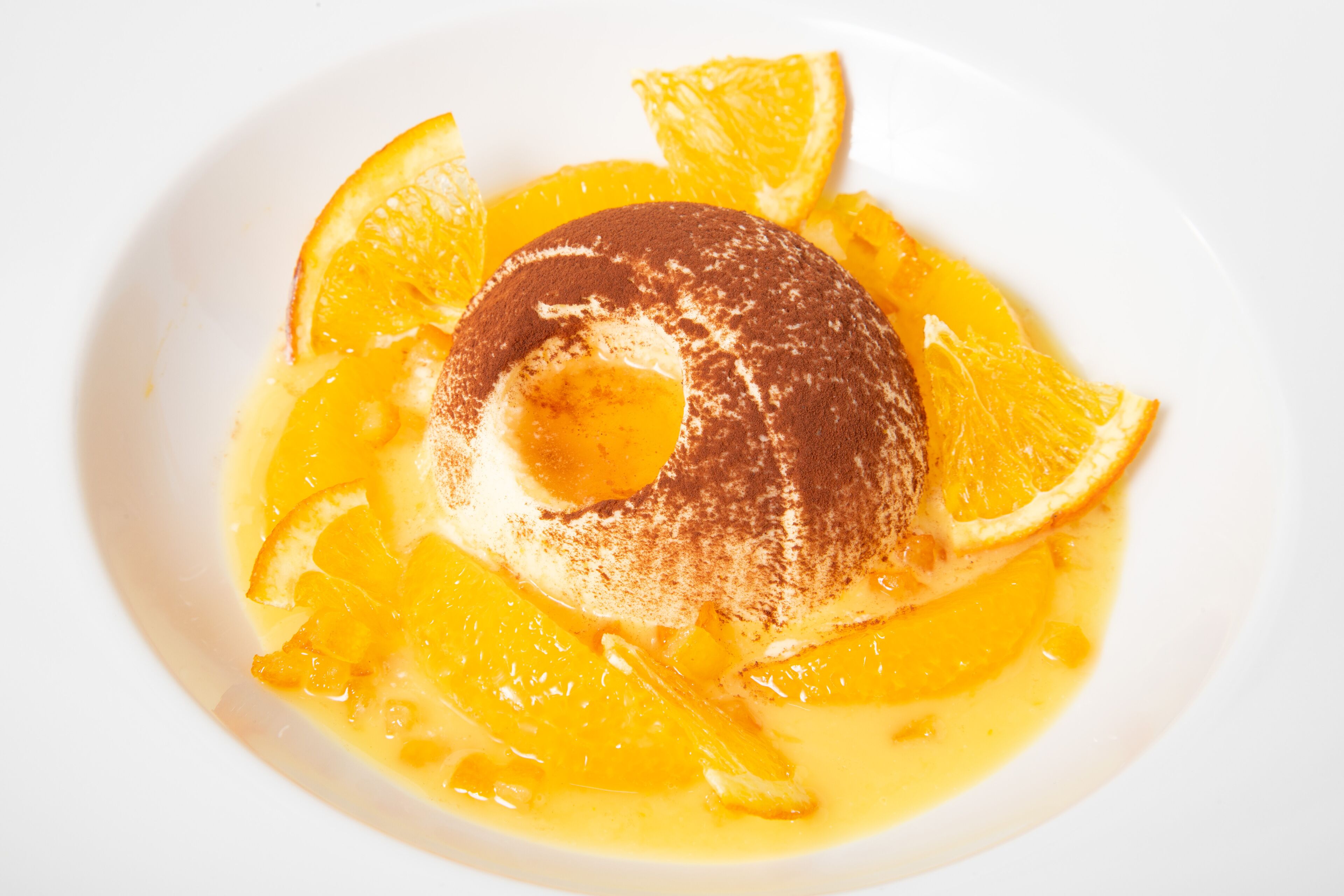 A dessert with a round shape, orange slices, and a dusting of a brown powder on top.