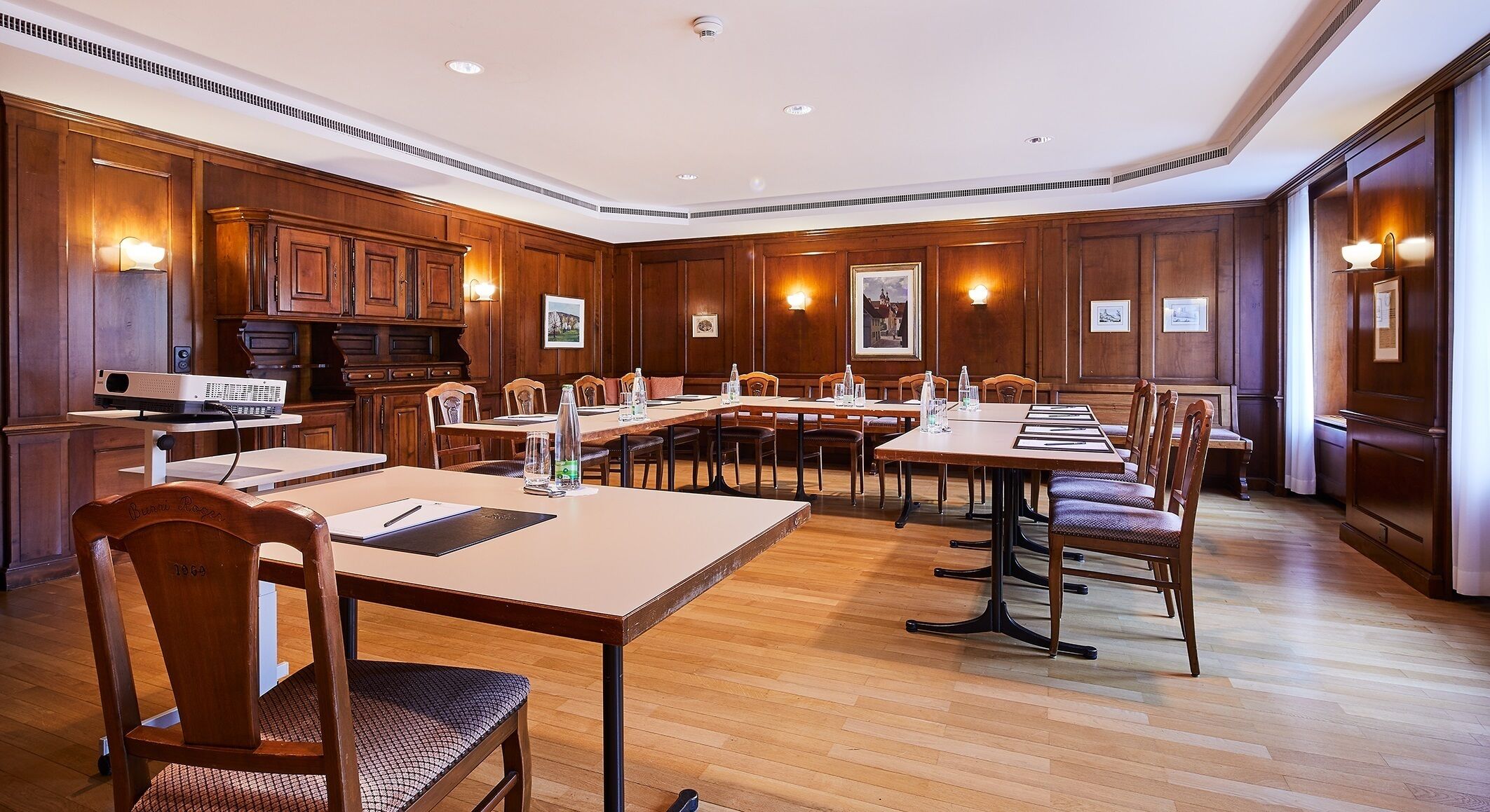 Un salón de conferencias con paneles de madera, varias mesas y sillas.
