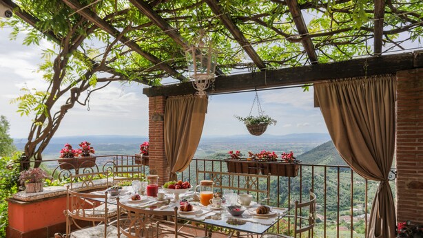 Una terraza con una mesa lista para el desayuno, con vistas a un paisaje montañoso.