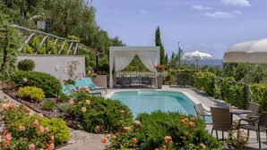 Zona de piscina con área de estar cubierta, sillas de descanso y vista al mar.