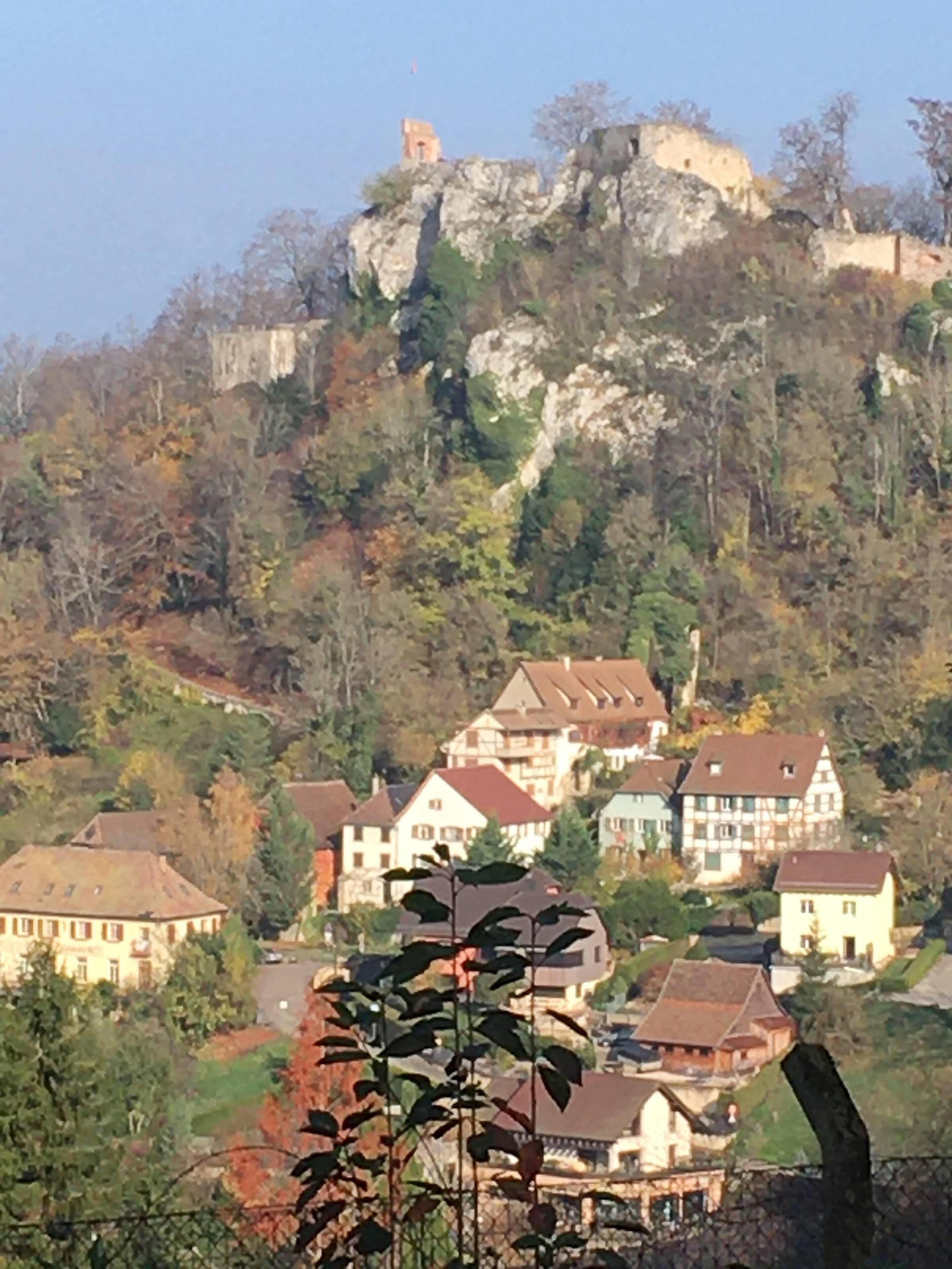 A hillside village with traditional houses, a prominent rock formation, and a small tower.