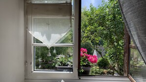 A window with a tissue box and a decorative vase on the sill, overlooking a garden with potted plants and a metal fence. - Maison des 5 Temps - Chambres Dhôtes de Charme à Ferrette (Ferrette)