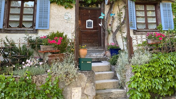 A rustic house with ivy-covered walls, a wooden front door, and a small garden with potted plants and flowers. - Maison des 5 Temps - Chambres Dhôtes de Charme à Ferrette (Ferrette)