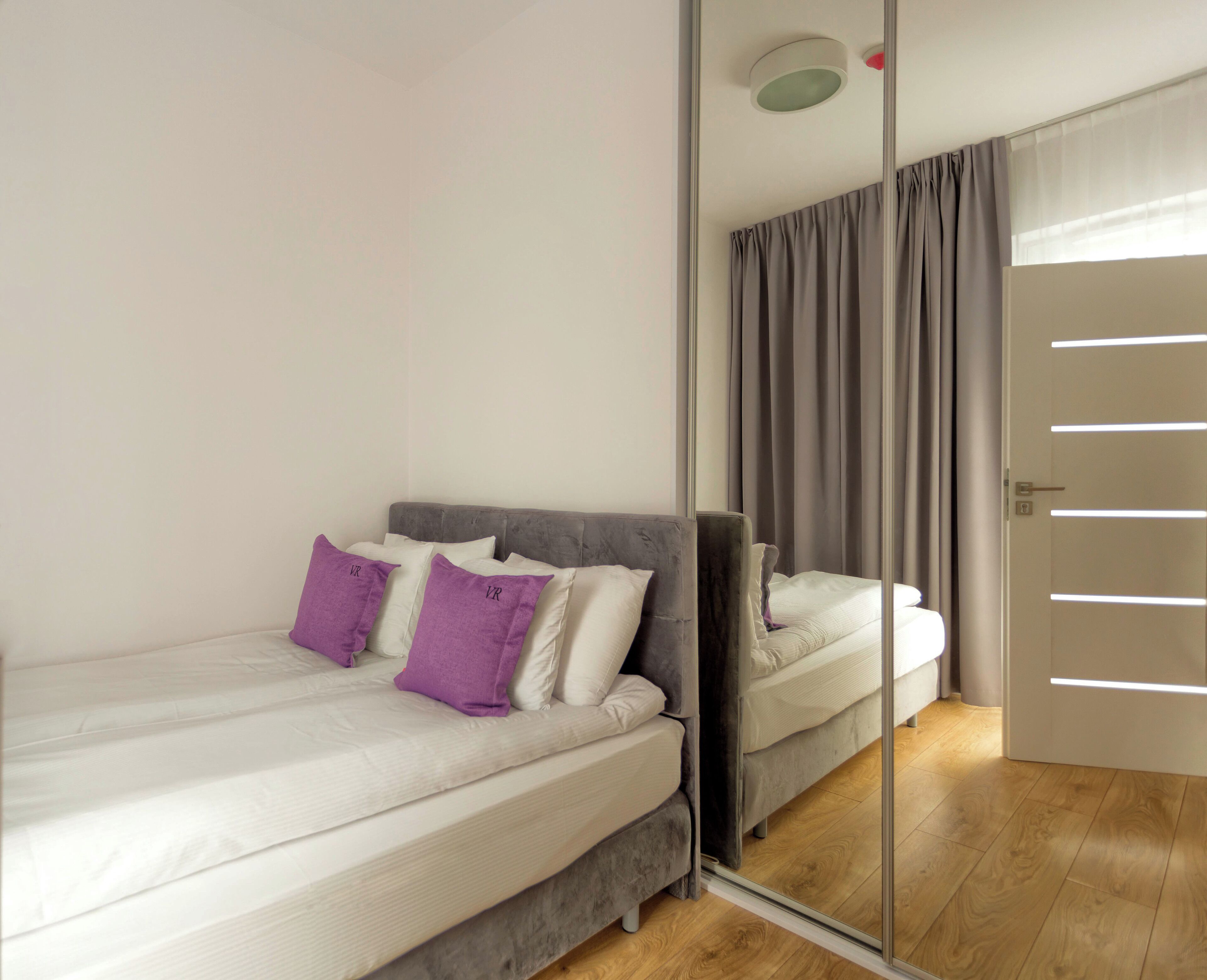 Quarto com uma cama, espelho e porta.