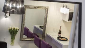 A modern room with a large mirror, purple chairs, a vase of flowers, a bottle of champagne, and a small table with a plate of food.