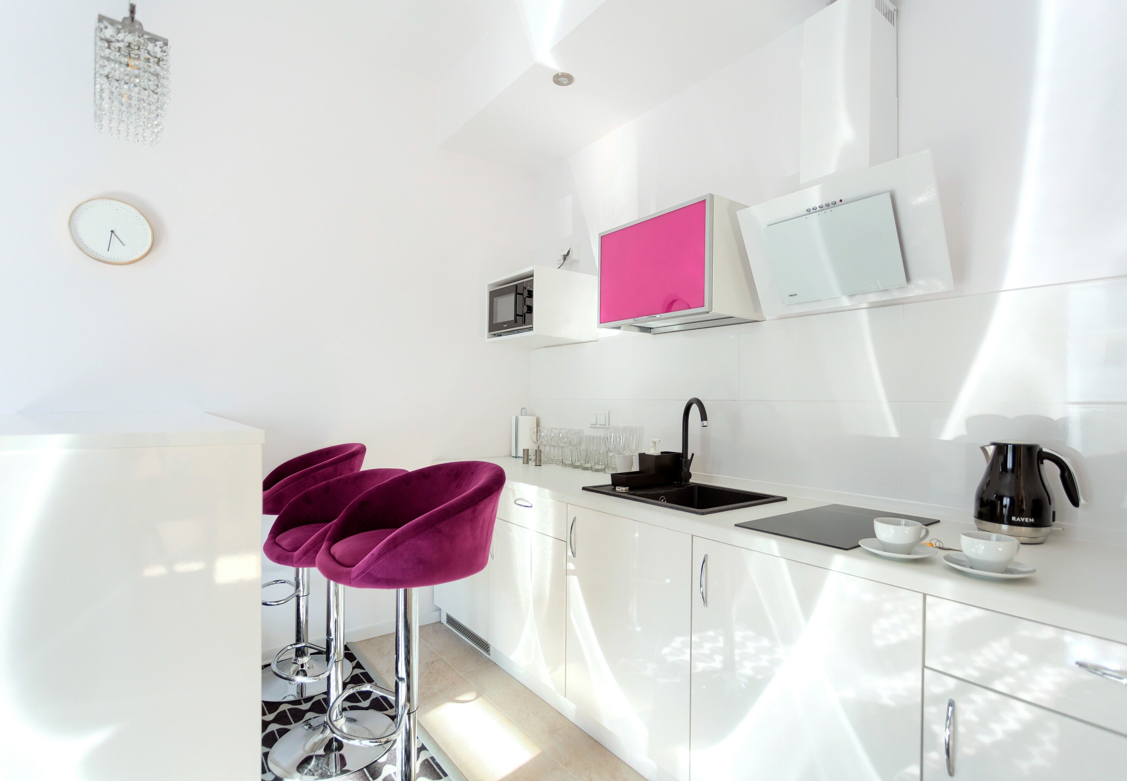 A modern kitchen with white cabinets, a black sink, a pink TV, and a coffee maker.