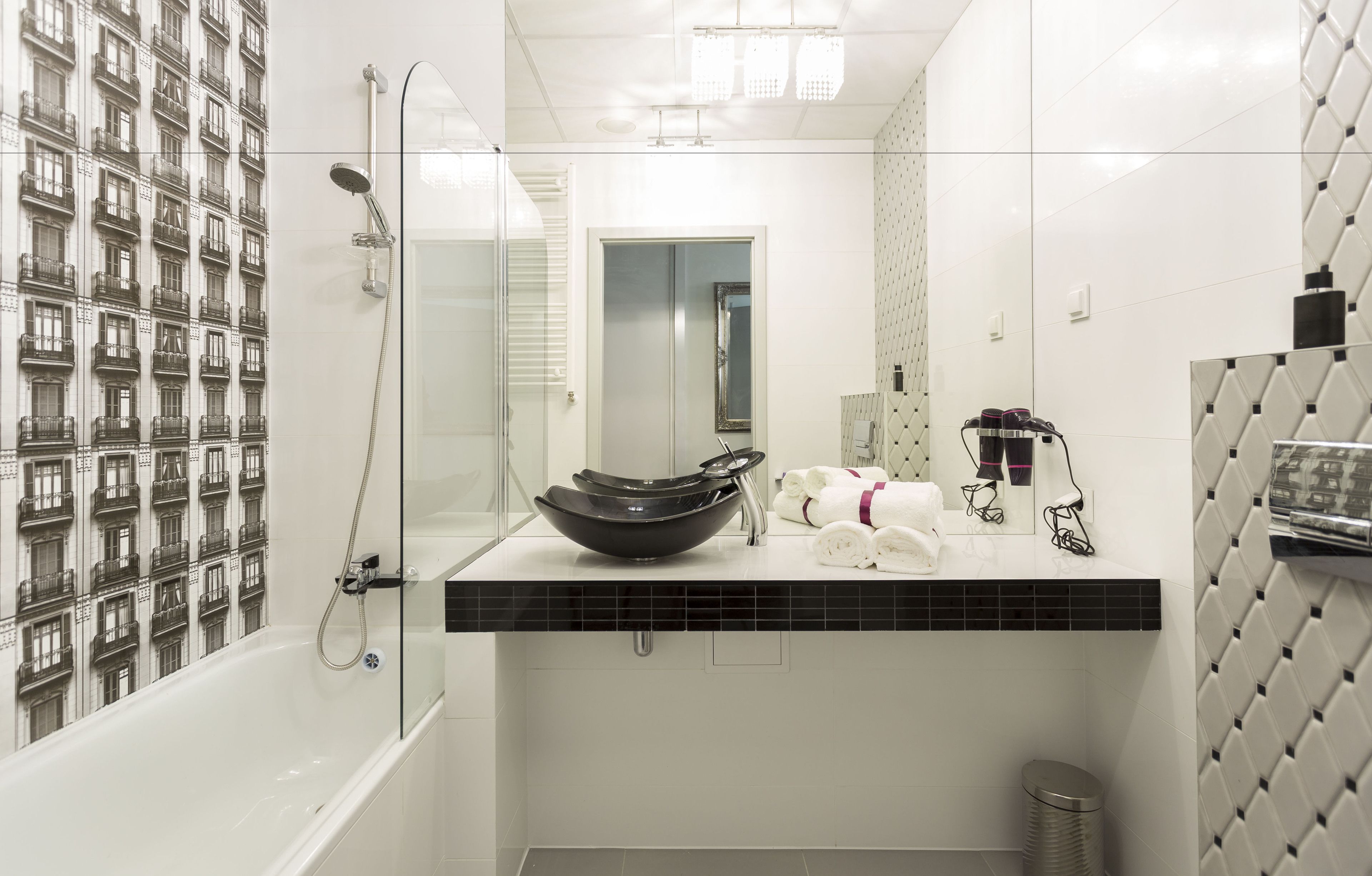 Een moderne badkamer met een douchecabine van glas, een zwart wastafelbakje op het aanrecht en een betegelde wand met een herhalend patroon.