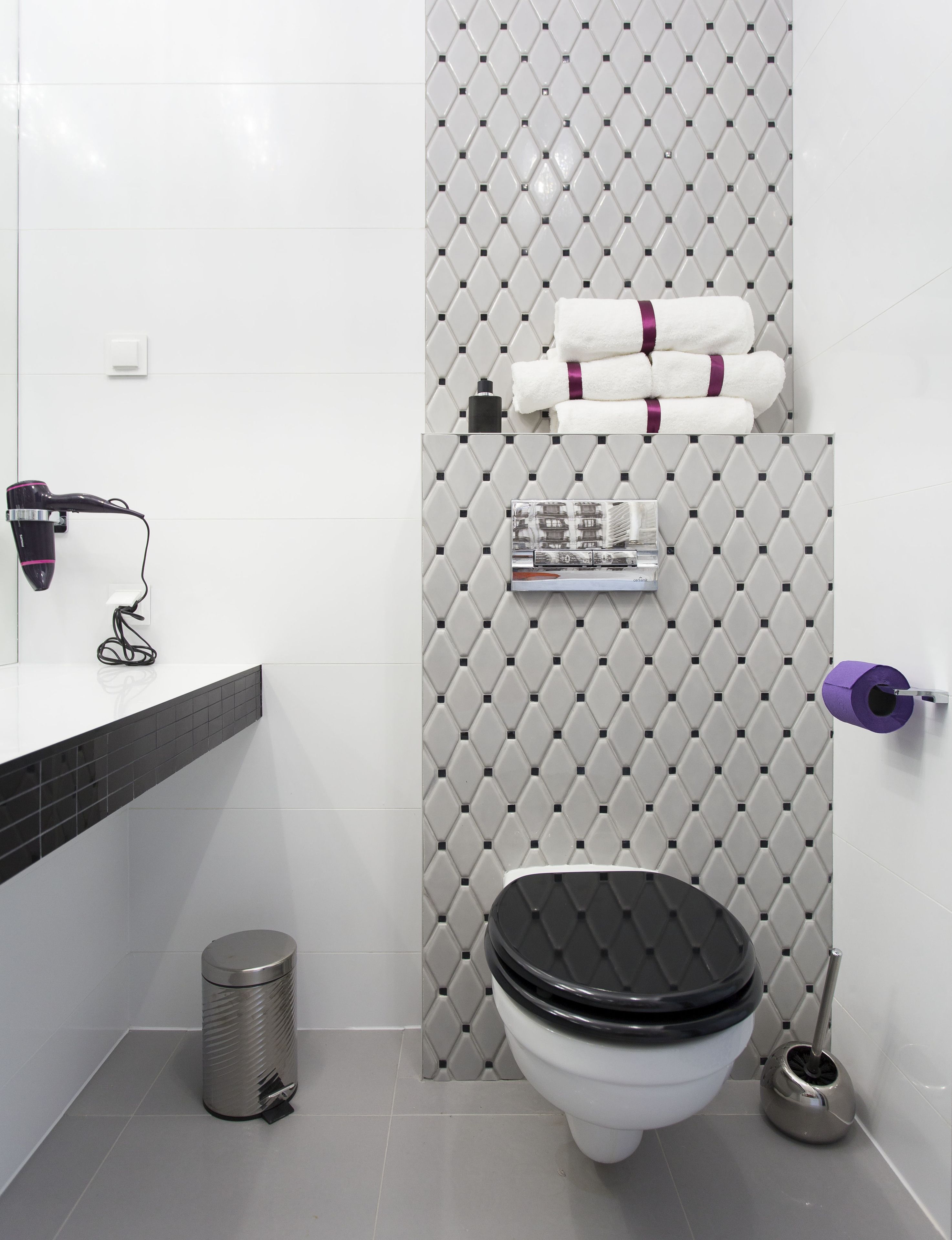 A modern bathroom with a toilet, bidet, trash can, and a hairdryer on a counter.