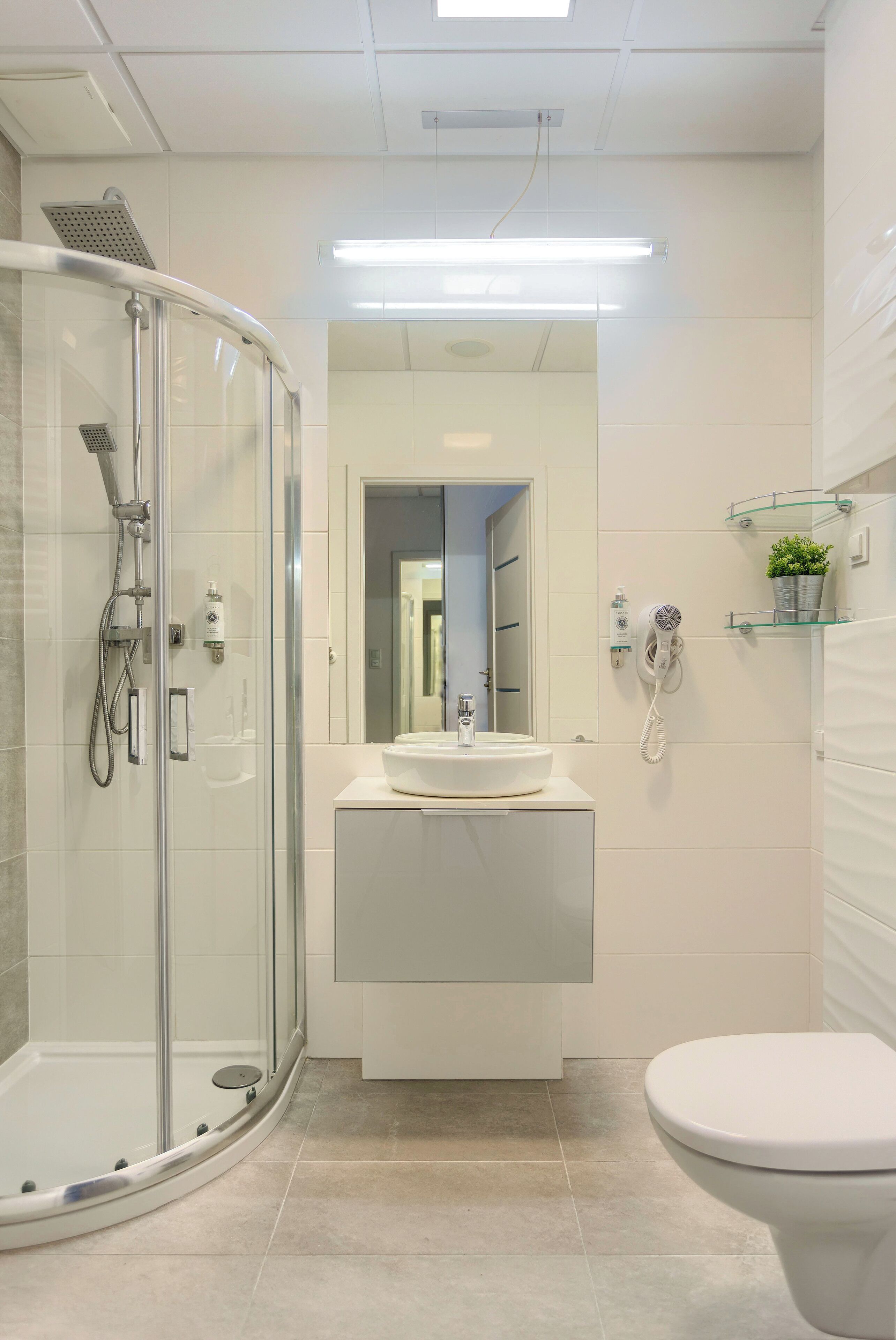 Un baño moderno con ducha de vidrio, lavabo con espejo e inodoro.