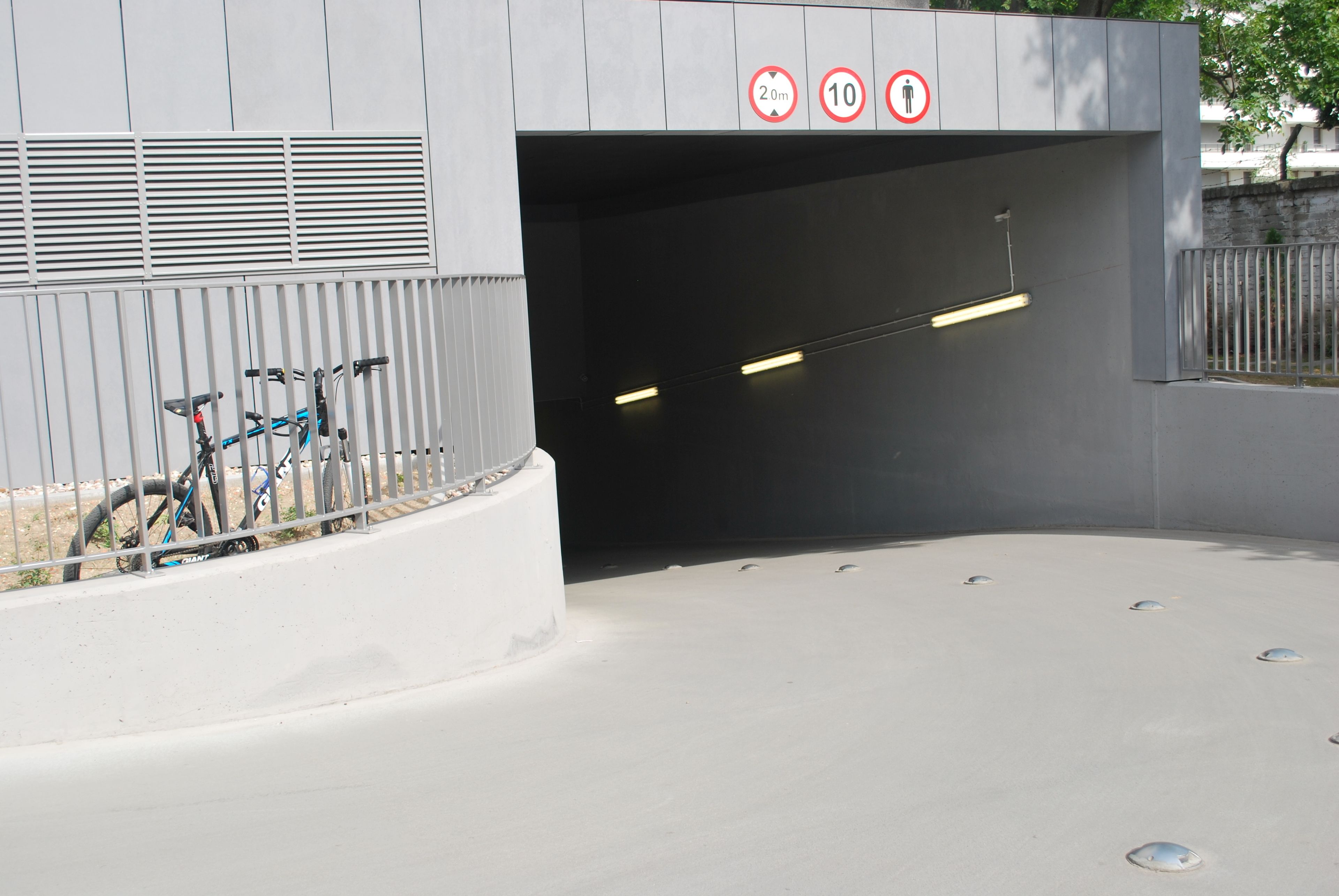 Un bâtiment moderne doté d’une entrée couverte, d’un support à vélos et d’un panneau indiquant une hauteur maximale de 20 mètres et de 10 mètres.