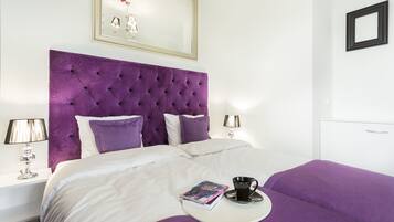A neatly made bed with a purple headboard, white bedding, and a book and cup on a tray.