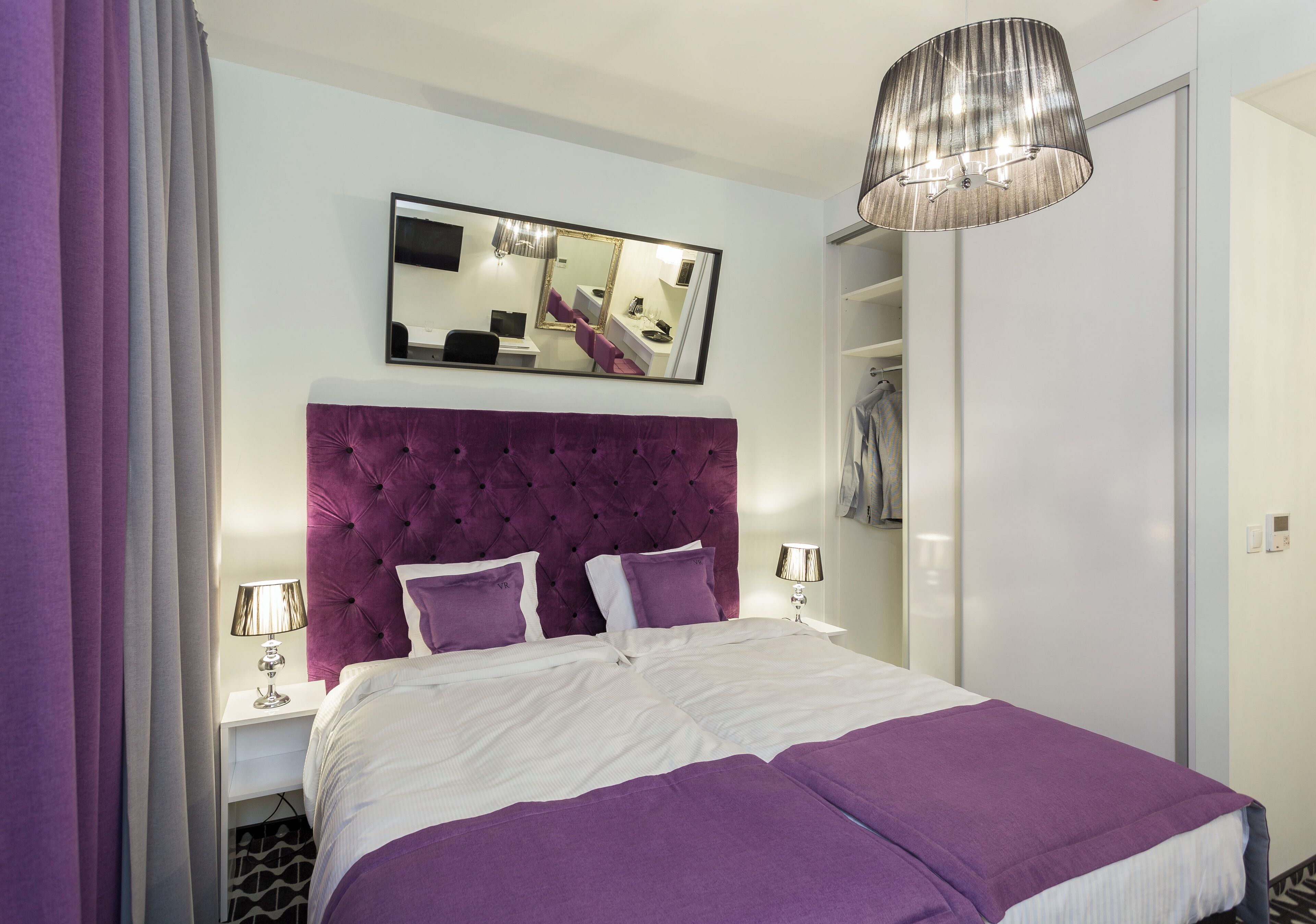 A bedroom with a large bed, a mirror, a wardrobe, and a hanging light fixture.