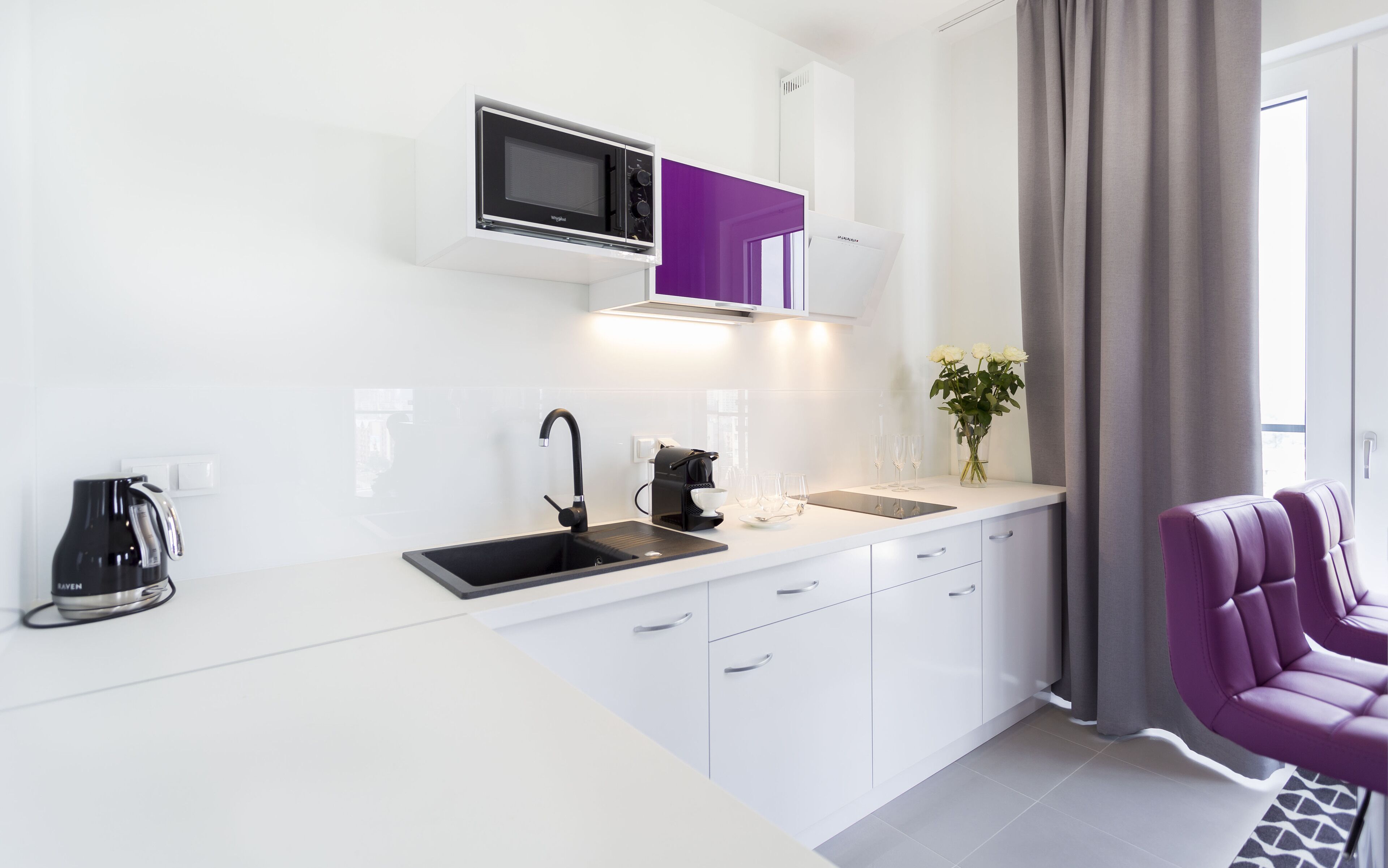 A modern kitchen with white cabinets, a black sink, a microwave, and a coffee maker.