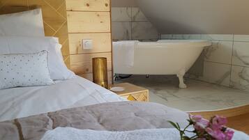 Ein Schlafzimmer mit Bett, Nachttisch, Lampe sowie einem Badezimmer mit Badewanne.