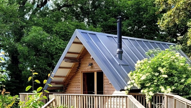 A wooden cabin with a sloped roof, a chimney, and a wooden deck with a railing. - Domaine de la Fauvrière (Sainte-Honorine-de-Ducy)