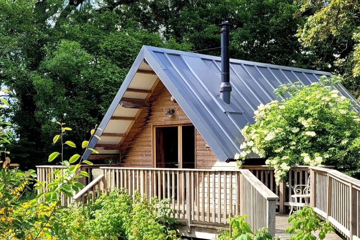 A wooden cabin with a sloped roof, a chimney, and a wooden deck with a railing.