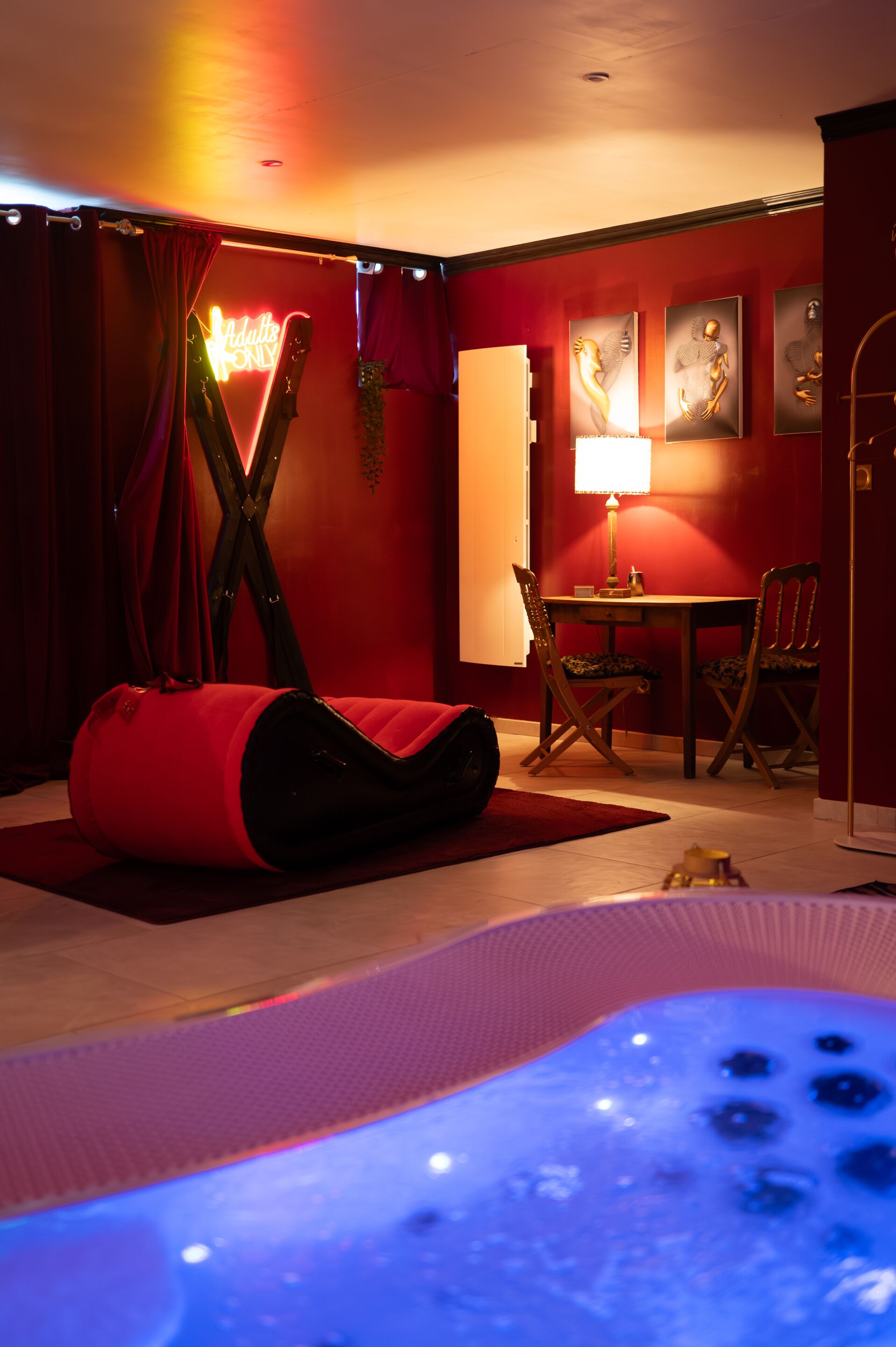 A room with a red wall, a massage chair, a table with chairs, and a hot tub.