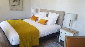 Un lit bien fait, avec une literie blanche et jaune, une tête de lit grise et deux tables de chevet avec des lampes.
